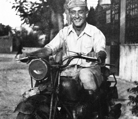 Happy Man on motorcycle in 1945. He is stationary in an urban road.