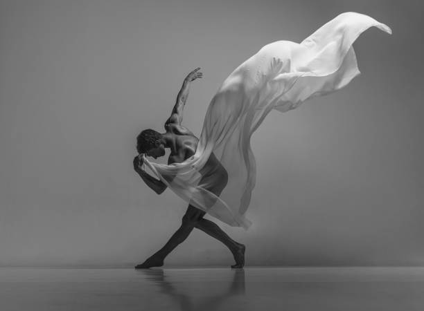 arte e bellezza del corpo maschile. ritratto in bianco e nero di un grazioso ballerino maschio muscoloso che balla con tessuto, stoffa isolata su sfondo grigio dello studio. - action balance ballet dancer ballet foto e immagini stock