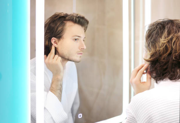 istock young man looking in the mirror,combing his hair,looking at problems on face. 1392502890