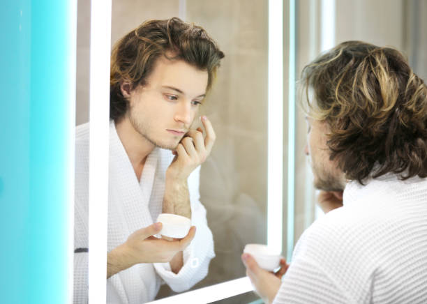 istock young man looking in the mirror,combing his hair,looking at problems on face. 1392502891