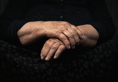 Wrinkled hands of a senior woman in a dark setting