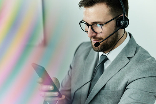 Side view of male trader using multiple computer screens while communicating through headphones at desk