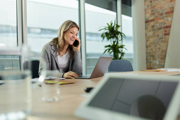 istock Happy businesswoman having a phone call while using laptop in the office. 1392506730