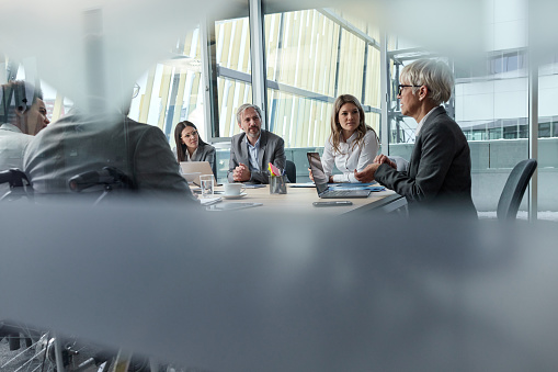 Senior businesswoman leading a meeting with group of her colleagues in the office. The view is through glass.