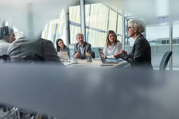 Business meeting in progress! Senior businesswoman leading a meeting with group of her colleagues in the office. The view is through glass. chief executive officer stock pictures, royalty-free photos & images