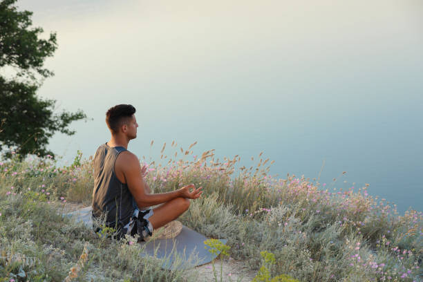 istock Man meditating in meadow near river. Space for text 1392513078