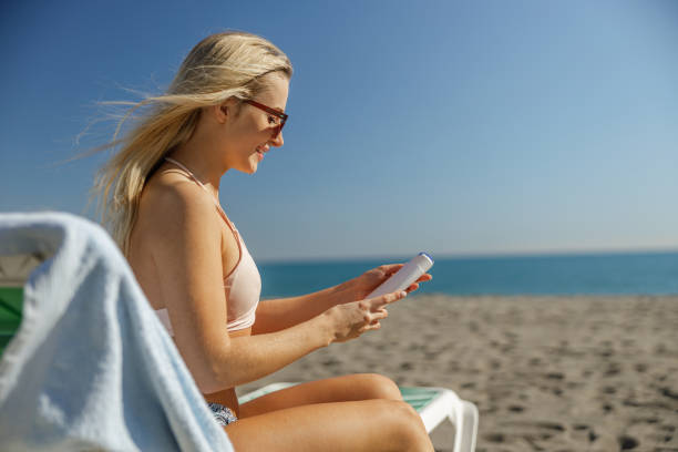 istock Smiling lady in sunglasses holding sunscreen body lotion while sunbathing 1392516312