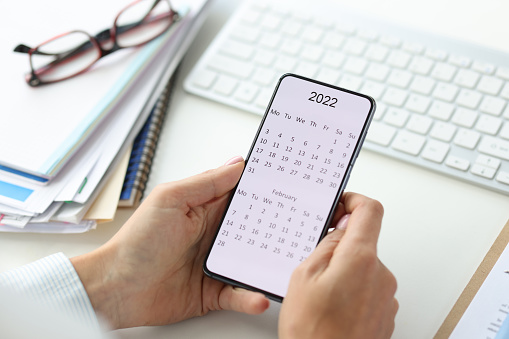 Person holding phone with calendar for 2022. Planning business tasks for year concept