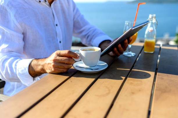 Mature man sitting at a cafe working on digital tablet by the sea