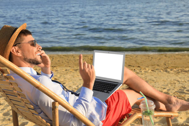 istock Man with laptop talking by mobile phone on beach. Business trip 1392519914