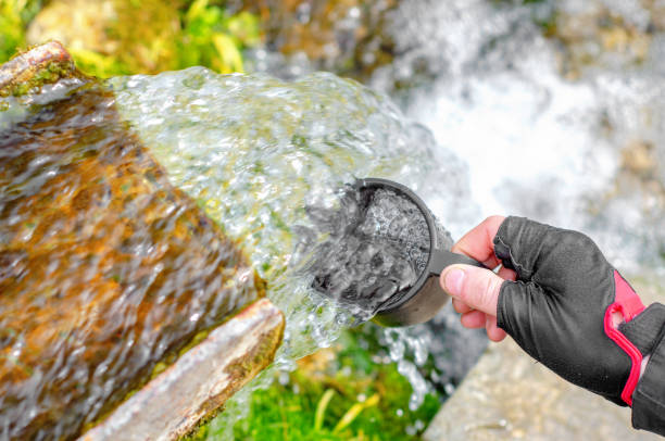 istock Refreshment with cold clean water on a hot summer day. The flow of clean water from the source. Human hand with a mug in the water. 1392523438