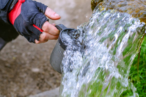 istock Refreshment with cold clean water on a hot summer day. The flow of clean water from the source. Human hand with a mug in the water. 1392523441