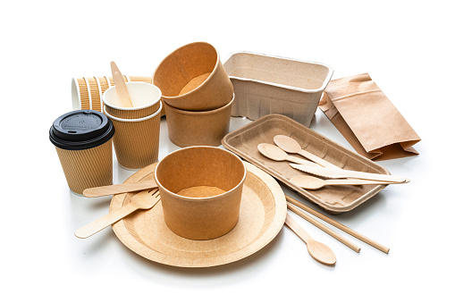 Sustainable lifestyle and environmental conservation background: plastic free eco friendly products shot from above on white background. The composition includes brown cardboard plate, bowl and cup, paper drinking straws, brown paper bag, wooden table knife, spoon and fork. High resolution 42Mp studio digital capture taken with SONY A7rII and Zeiss Batis 40mm F2.0 CF lens
