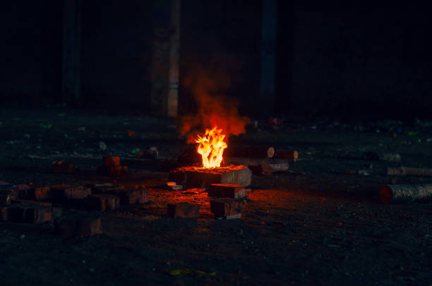 istock Lighting a fire on a stone at night. Small red fire, smoke from the flames, scattered firewood. 1392524765