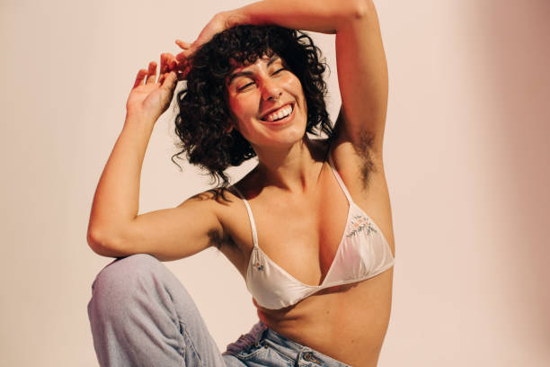 Unshaven young woman smiling cheerfully while wearing a bra Unshaven young woman smiling cheerfully while wearing a bra and jeans. Happy young woman embracing her natural body and underarm hair. Body positive young woman making her own choice about her body. body hair stock pictures, royalty-free photos & images