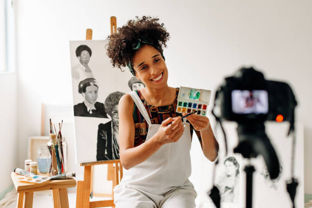 Painter recording an art tutorial in a studio Painter recording an art tutorial in her studio. Happy young female painter smiling while live streaming with a camera. Young female freelancer creating a video blog in her art studio. art class photos stock pictures, royalty-free photos & images