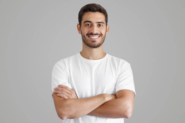 retrato de un hombre guapo y sonriente con camiseta blanca, de pie con los brazos cruzados - caucasian fotografías e imágenes de stock