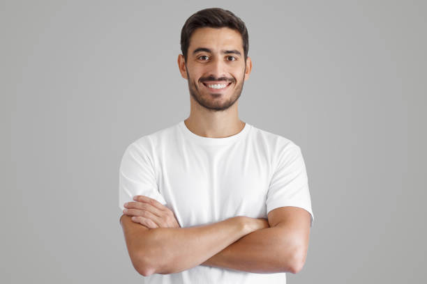 하얀 티셔츠를 입고 웃고 있는 잘생긴 남자의 초상화, 교차된 팔로 서 있는 모습 - 남자 이미지 뉴스 사진 이미지