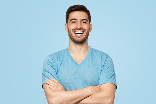 Young handsome man in blue t-shirt, standing with crossed arms and laughing at funny joke