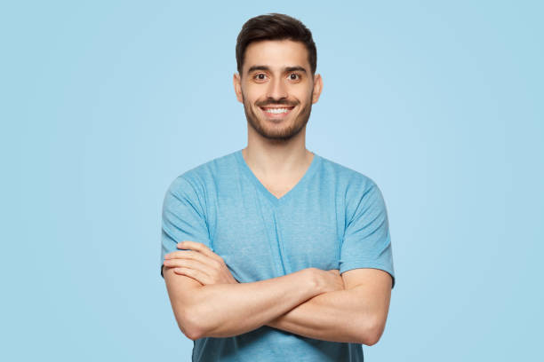 istock Young handsome man wearing blue tshirt, standing with crossed arms 1392528350