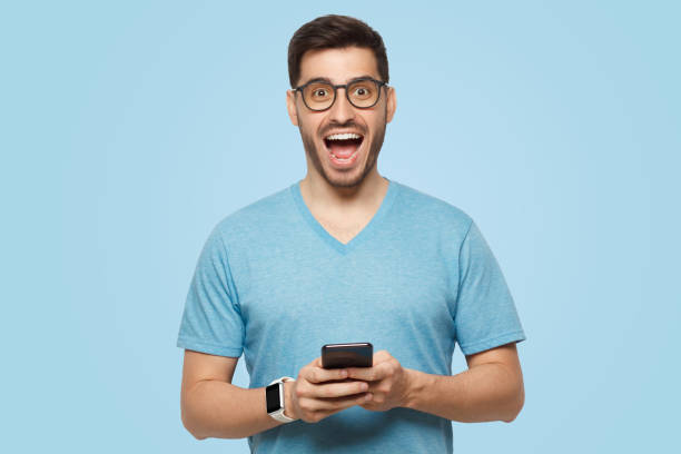 istock Young handsome man holding phone in hands, looking at camera with excited WOW face 1392528361