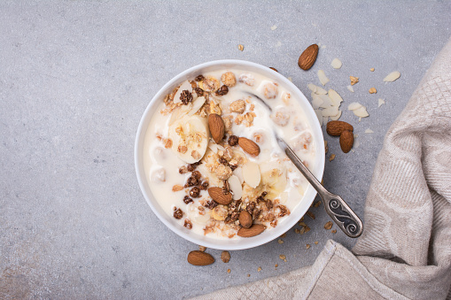 Top view of granola with yogurt, fresh banana and almond nuts for healthy breakfast on grey concrete background