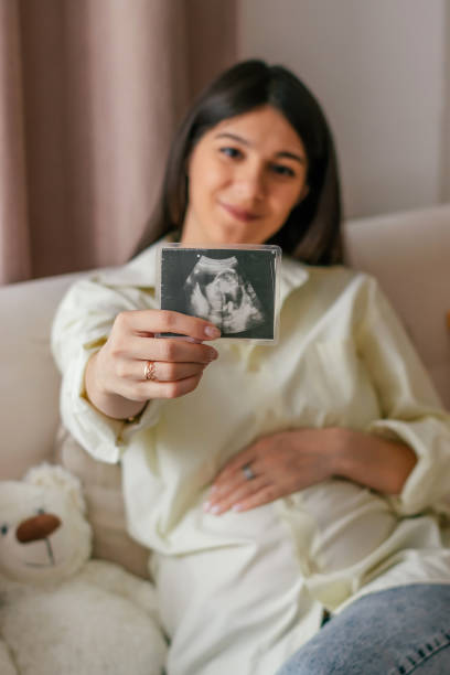 Blurry young pregnant woman in a yellow shirt and jeans shows ultrasound photo.Pregnancy and prenatal healthcare concept. stock photo