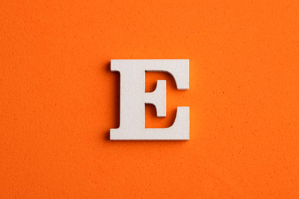 istock Alphabet letter E - White wood piece on orange foamy background 1392529440