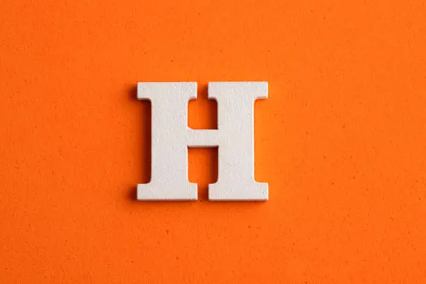 Alphabet letter H - White wood piece on orange foamy background