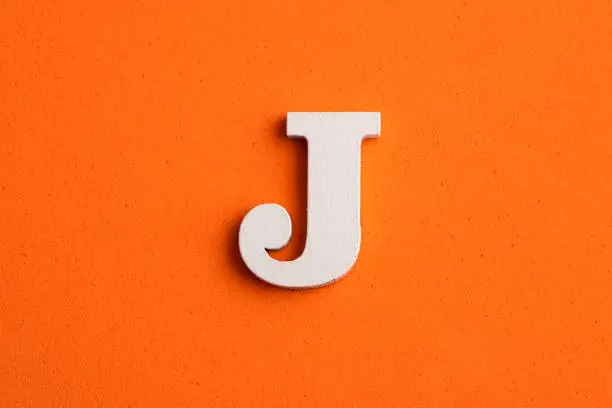 Alphabet letter J - White wood piece on orange foamy background