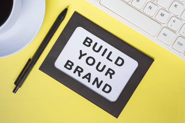 istock Build your brand text on white note with yellow sheet on wooden desk. 1392532677