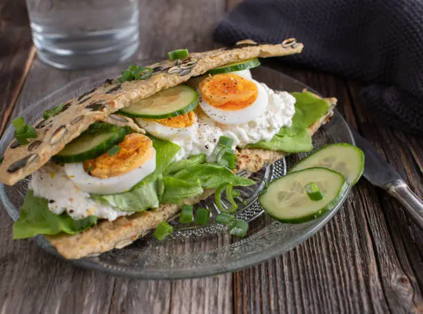 Fitness sandwich made with oatmeal pancake and filled with cottage cheese, boiled eggs and vegetables. Served on a plate. Ready to eat.