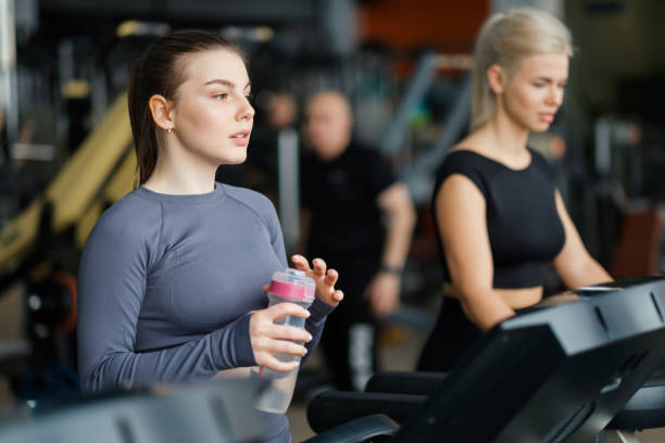 Two beautiful caucasian girls run on a treadmill in the gym. stock photo