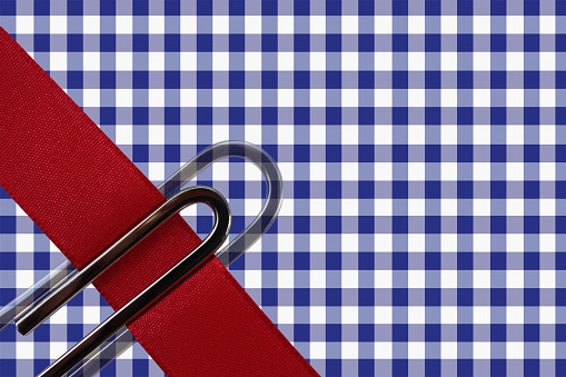 Paper clip on red ribbon on blue checkered tablecloth background