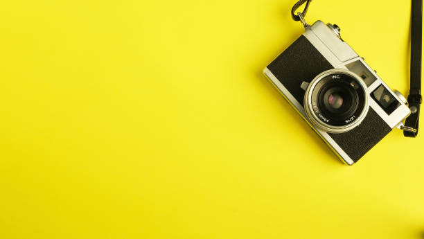 istock Vintage camera on yellow background, old strap camera with old lens, souvenir camera with camera film, isolated close-up retro photography cam top view 1392538758