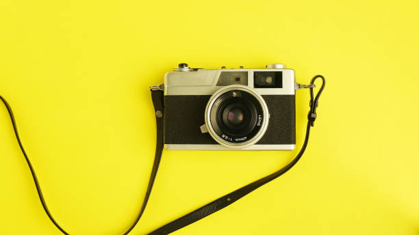 istock Vintage camera on yellow background, old strap camera with old lens, souvenir camera with camera film, isolated close-up retro photography cam top view 1392538792