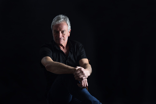 front  view portrait of senior man sitting on chair on black background