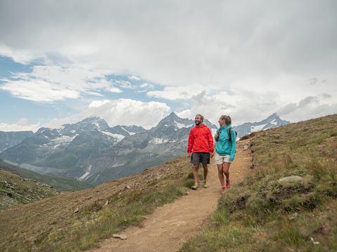 View of couple hiking on mountain trail looking at spectacular Matterhorn peak, Switzerland