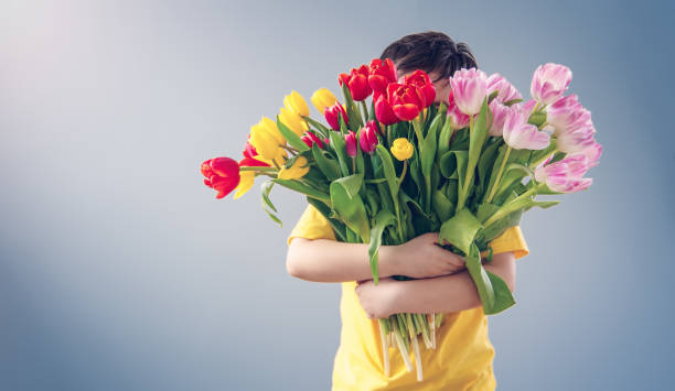 uroczy chłopiec stojący w pomieszczeniu z bukietem kolorowych tulipanów. - flower spring bouquet child zdjęcia i obrazy z banku zdjęć