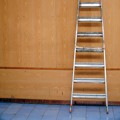 A folded aluminum stepladder stands against the wall