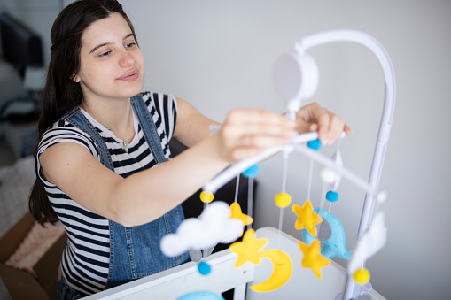 Pregnant woman adjusting cot mobile toy in nursery bedroom for her baby soon to be delivered.