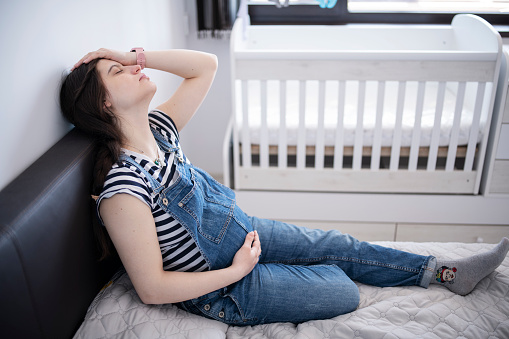 Young pregnant woman on the bed having stomach ache and headache.