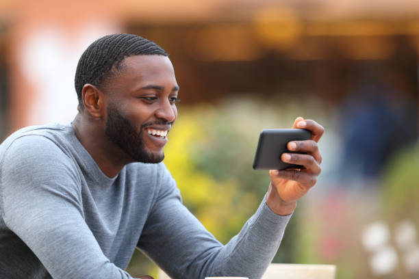 Man with black skin watching media on smart phone in a bar stock photo