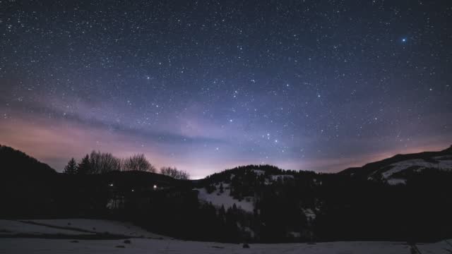 Magic blue night sky with million stars of milky way galaxy and sunrise in winter mountains nature Night to Day Time lapse