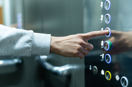 Closeup of person's hand pushing button to select first floor in elevator. Passenger lift. Businessman in office. Movement within building concept
