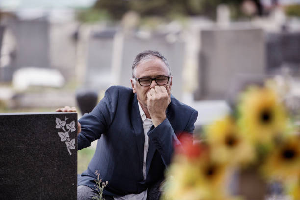 Middle-aged man in front of graves in a cemetery A middle-aged man in front of graves in a cemetery looking sad burial mound photos stock pictures, royalty-free photos & images