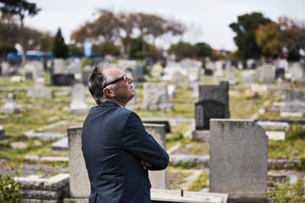 A middle-aged man stands in front of graves in a cemetery looking up. A middle-aged man in front of graves in a cemetery looking up. burial mound photos stock pictures, royalty-free photos & images