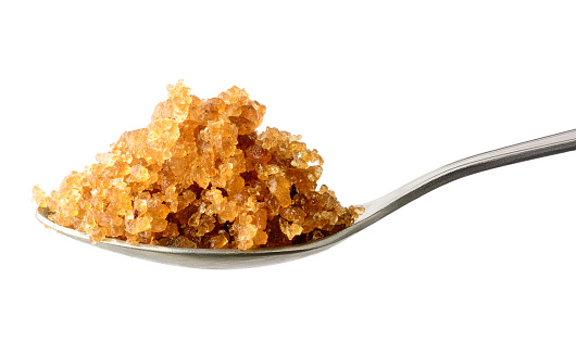 palm sugar candy or rock candy in a spoon, lump sugar made by tapping the sap from the inflorescence of the palm tree, on white background, medicinal food used for dry persistent cough