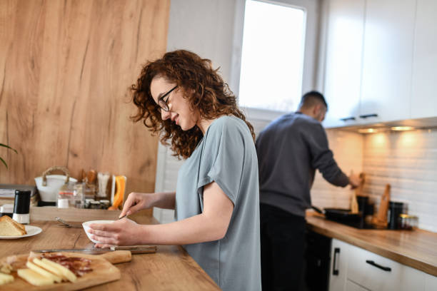 mężczyzna podgrzewa patelnię, podczas gdy dziewczyna bije jajka na omlet i przygotowuje ser - on eggs standing spoon zdjęcia i obrazy z banku zdjęć