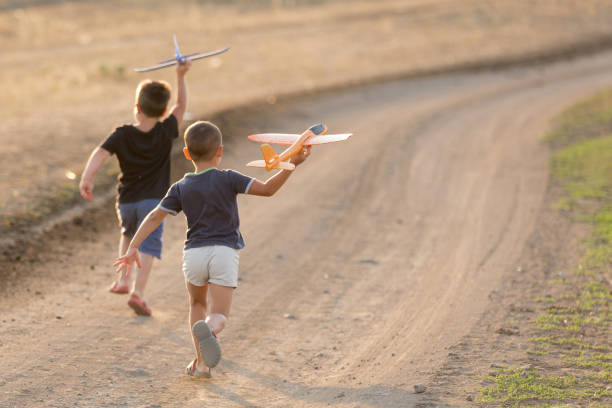 おもちゃの飛行機を起動する未舗装の道路を走る2人の小さな男の子、夏の屋外ゲーム - group of people people family multi ethnic group ストックフォトと画像